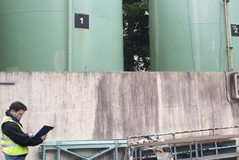 two large tanks with a consultant in hi vis holding a clipboard