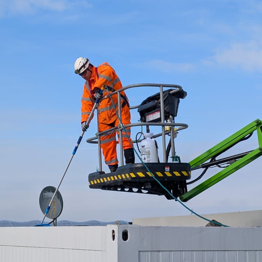 field engineer wearing protective clothing using cherry picker lift to disinfect roof of a building 