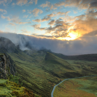 field with a road running through it with sunset behind clouds
